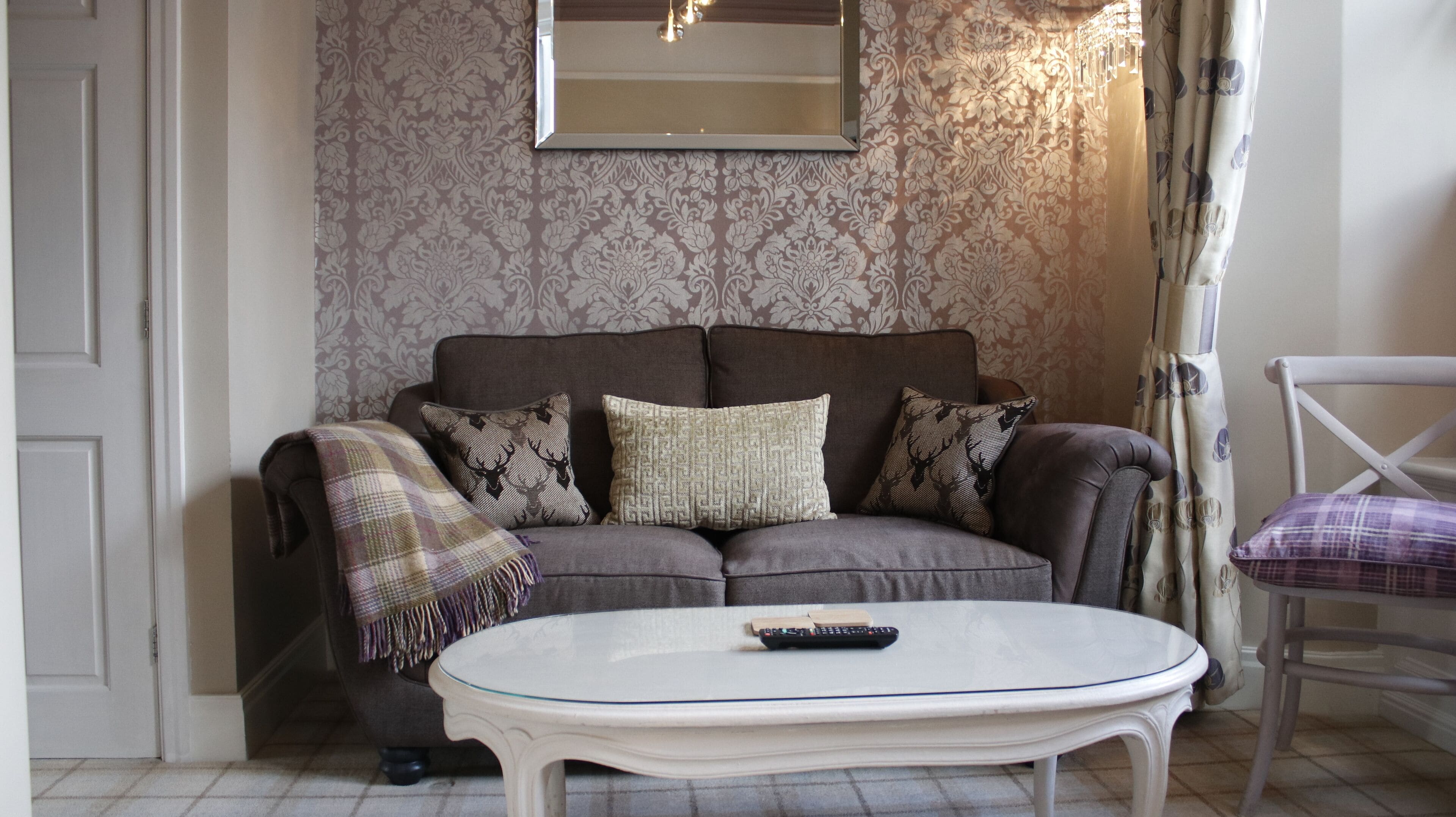 Ein Wohnzimmer mit einem grauen Sofa, zwei gemusterten Kissen, einer Karo-Decke und einem weißen Couchtisch mit Fernbedienung.