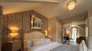 A bedroom with a large bed, a nightstand, a dresser, a framed picture on the wall, and a chandelier. - Bowness Bay Suites - Adults only (Windermere)