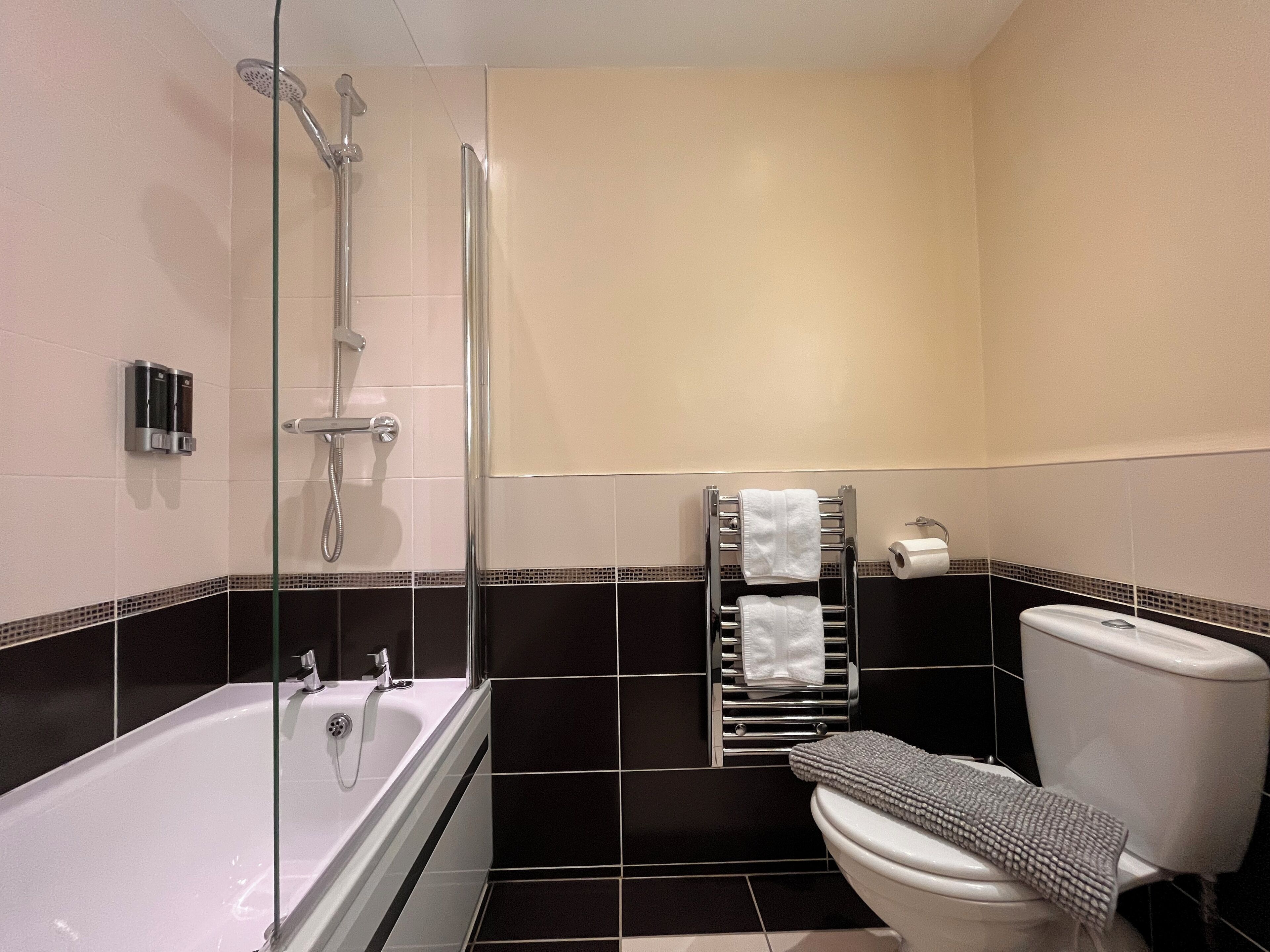 Een moderne badkamer met bad, douche, toilet en handdoekhouder.
