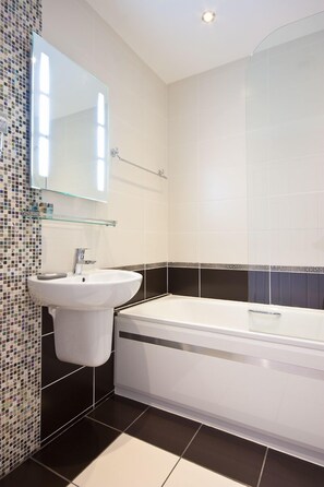 A modern bathroom with a white sink, a glass mirror, and a bathtub.
