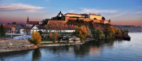 A historic castle on a riverbank with a prominent tower, surrounded by autumn foliage and a calm river.
