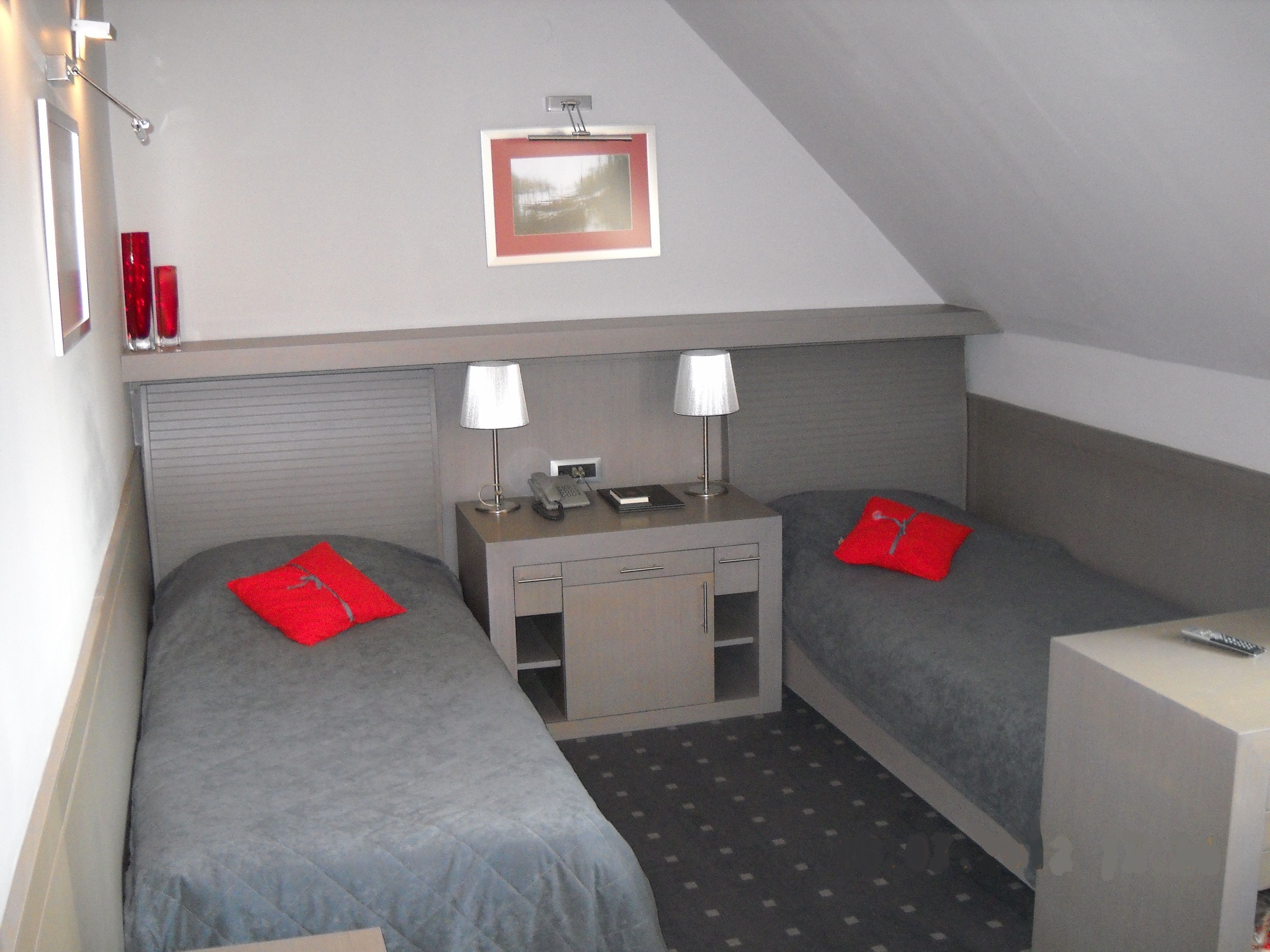 A small, triangular room with two single beds, a desk with a lamp, and a small table with a telephone.