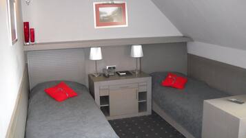 A small, triangular room with two single beds, a desk with a lamp, and a small table with a telephone.