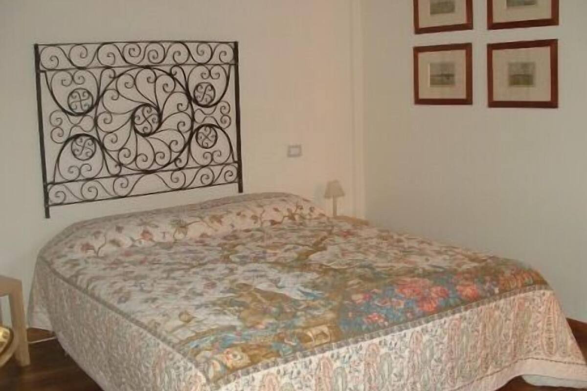 A bedroom with a floral-patterned bedspread, a decorative metal headboard, and framed pictures on the wall.