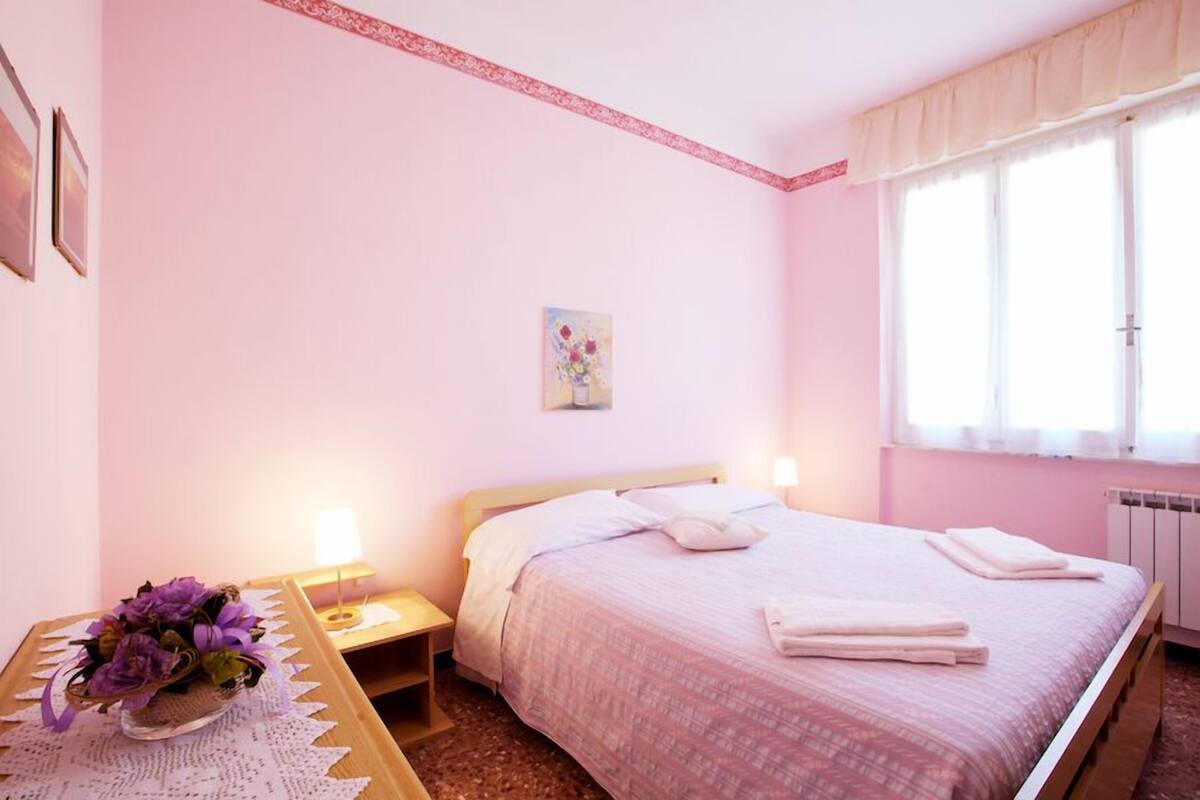 A bedroom with a bed, bedside table, lamp, and a window with curtains.