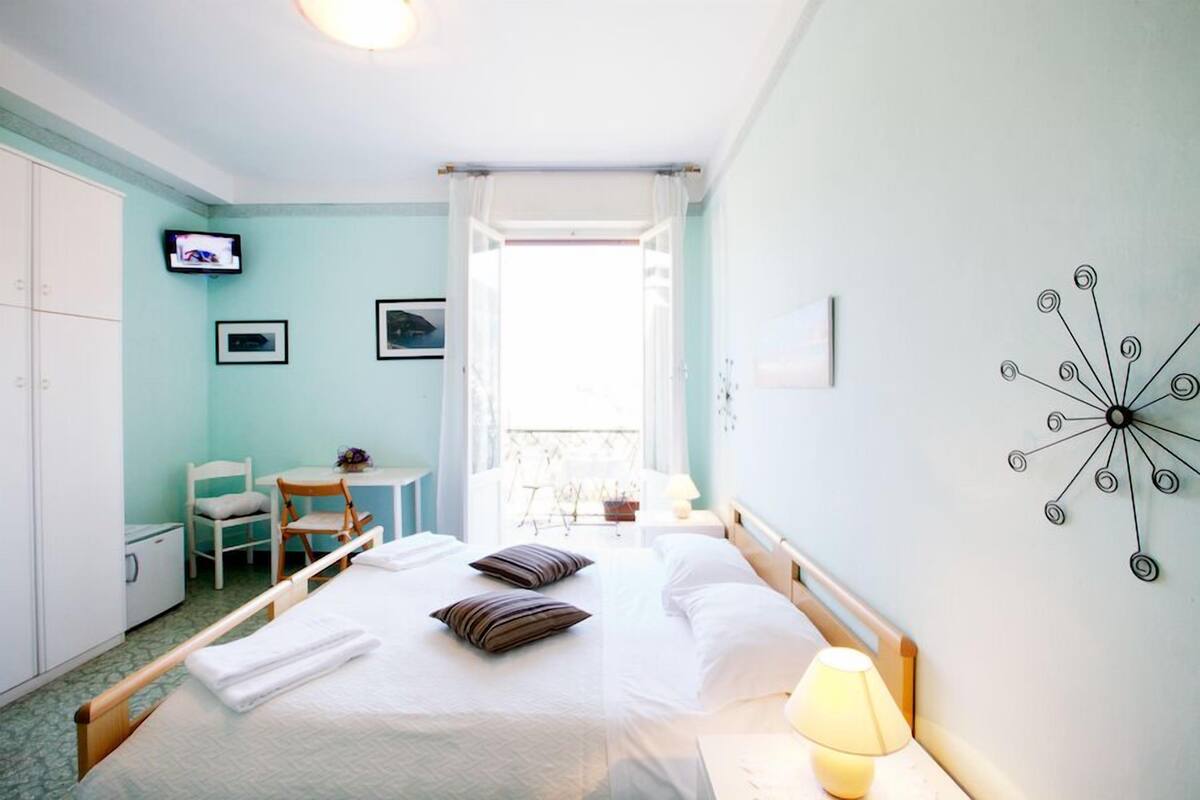 A hotel room with a bed, a desk, a chair, a TV, and a balcony with a view.