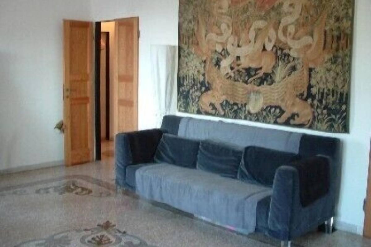 A room with a blue sofa, a patterned rug, and a large tapestry on the wall.