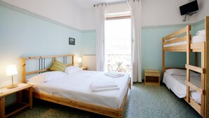 A hotel room with a wooden bed, a bedside table with a lamp, a small bedside table, a bunk bed, and a TV mounted on the wall. - La Perla Blu (Levanto)