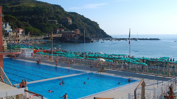 A swimming pool area with multiple pools, a bridge, and a hillside with buildings. - La Perla Blu (Levanto)