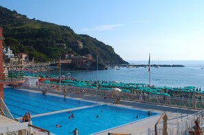 A swimming pool area with multiple pools, a bridge, and a hillside with buildings. - La Perla Blu (Levanto)