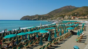 A beach with rows of sun loungers and umbrellas, a clear blue sky, and a mountainous backdrop. - La Perla Blu (Levanto)