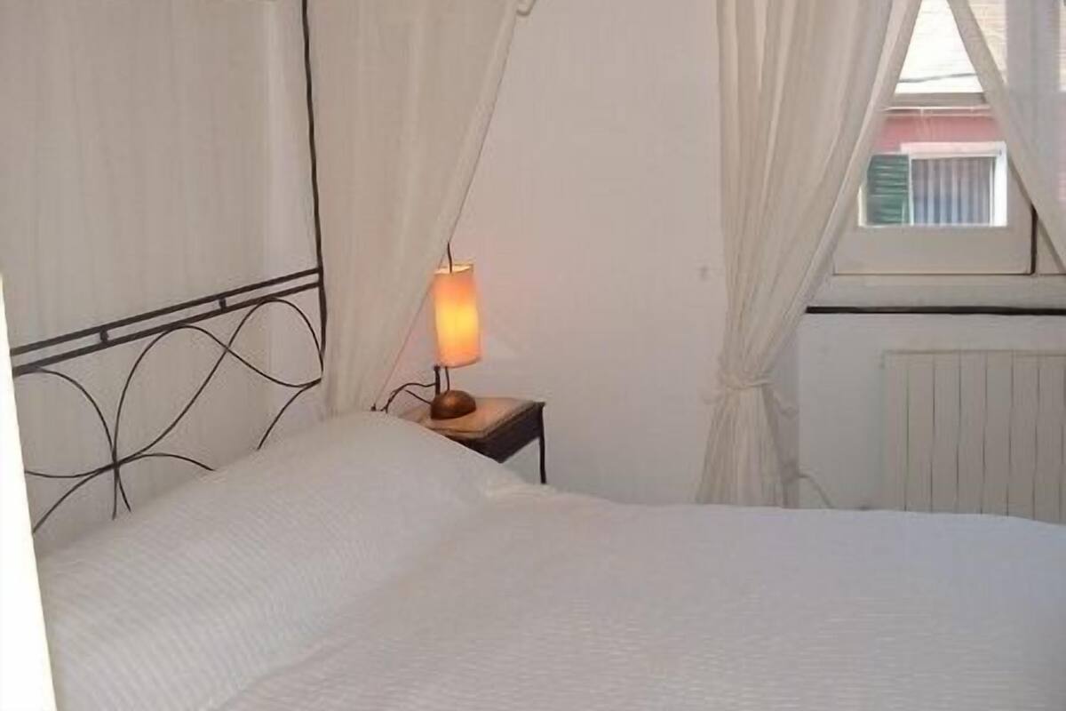 A bedroom with a bed, a bedside lamp, a window with curtains, and a radiator.