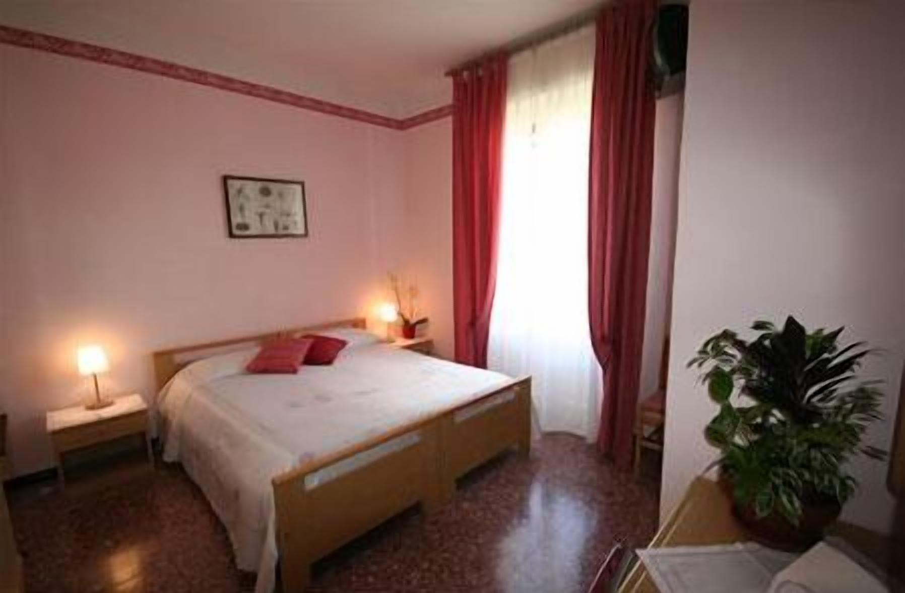 Una camera da letto con un letto di legno, due comodini, un tavolino e una pianta in vaso, con una finestra e tende rosse.