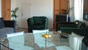 A living room with a glass dining table, green sofas, a TV, and a door. - La Perla Blu (Levanto)