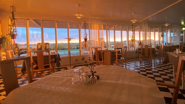 A dining area with a checkered floor, large windows with a view of the outdoors, and a table set for two with a vase of flowers. - Kvarnens Pensionat och Bed & Breakfast (Falkenberg)