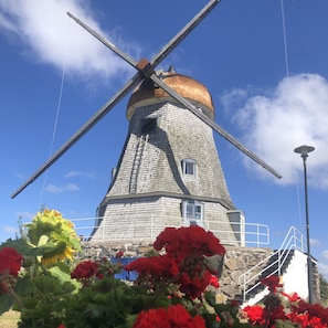 A windmill with a stone base and a wooden top, surrounded by red flowers and a clear blue sky. - Kvarnens Pensionat och Bed & Breakfast (Falkenberg)