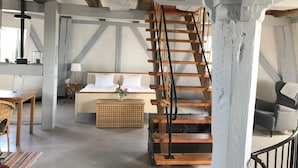 A rustic room with a wooden staircase, a bed with white linens, a wooden table, and a wicker chair. - Kvarnens Pensionat och Bed & Breakfast (Falkenberg)
