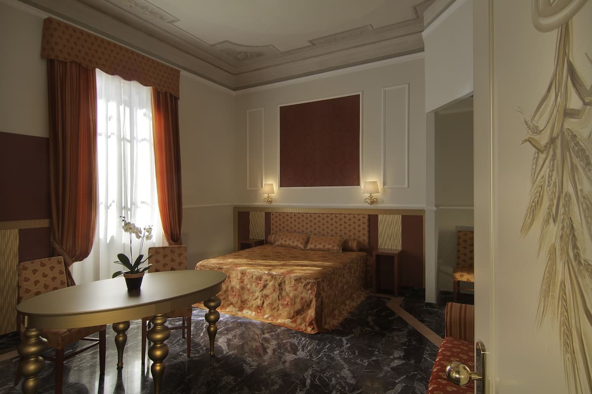 A hotel room with a large bed, a dining table, and a potted plant.