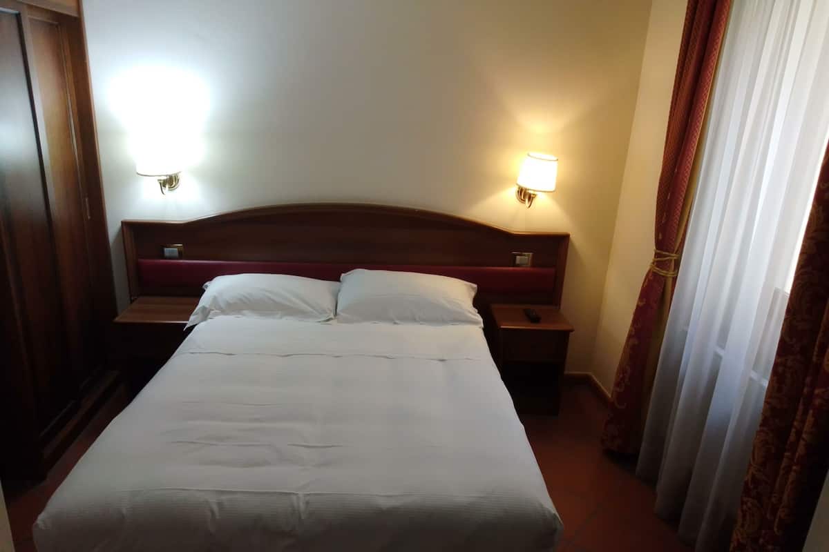 A hotel room with a large bed, two bedside tables, and two wall-mounted lamps.