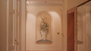 A hallway with wooden flooring, white walls, and a floral arrangement on a pedestal. - Relais la Corte di Cloris (Florence)