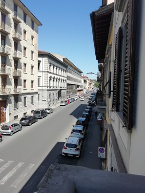 Vista callejera con coches aparcados, edificios con balcones y un cielo azul despejado.