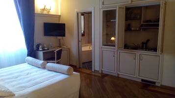 A hotel room with a bed, a desk with a chair, a television, a bathroom, and a kitchenette.