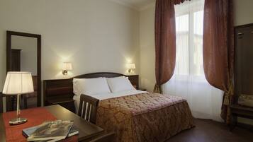 A hotel room with a bed, bedside lamps, a desk with a lamp, a chair, and a window with curtains.