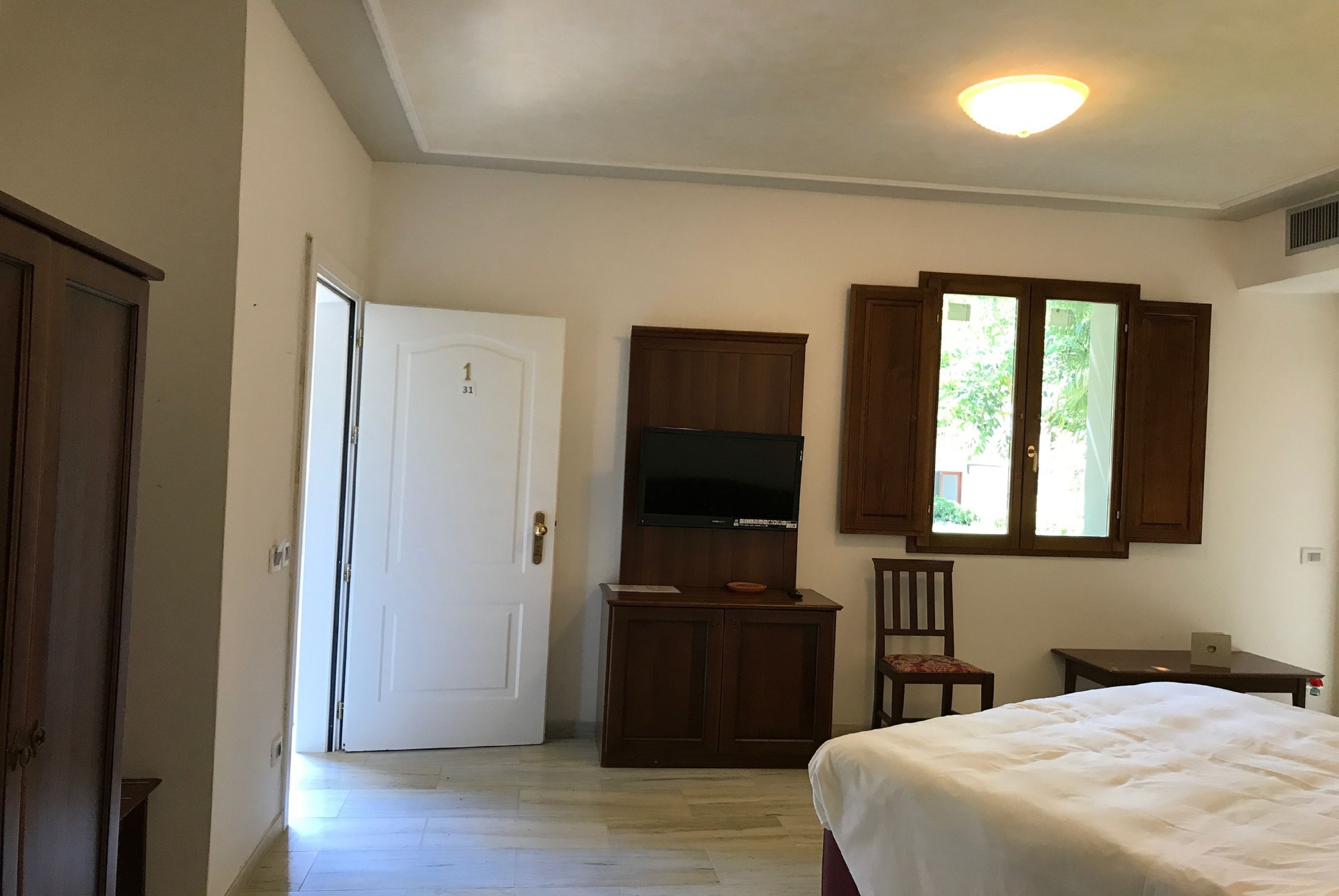 A bedroom with a bed, a desk, a chair, a TV, and a wardrobe.