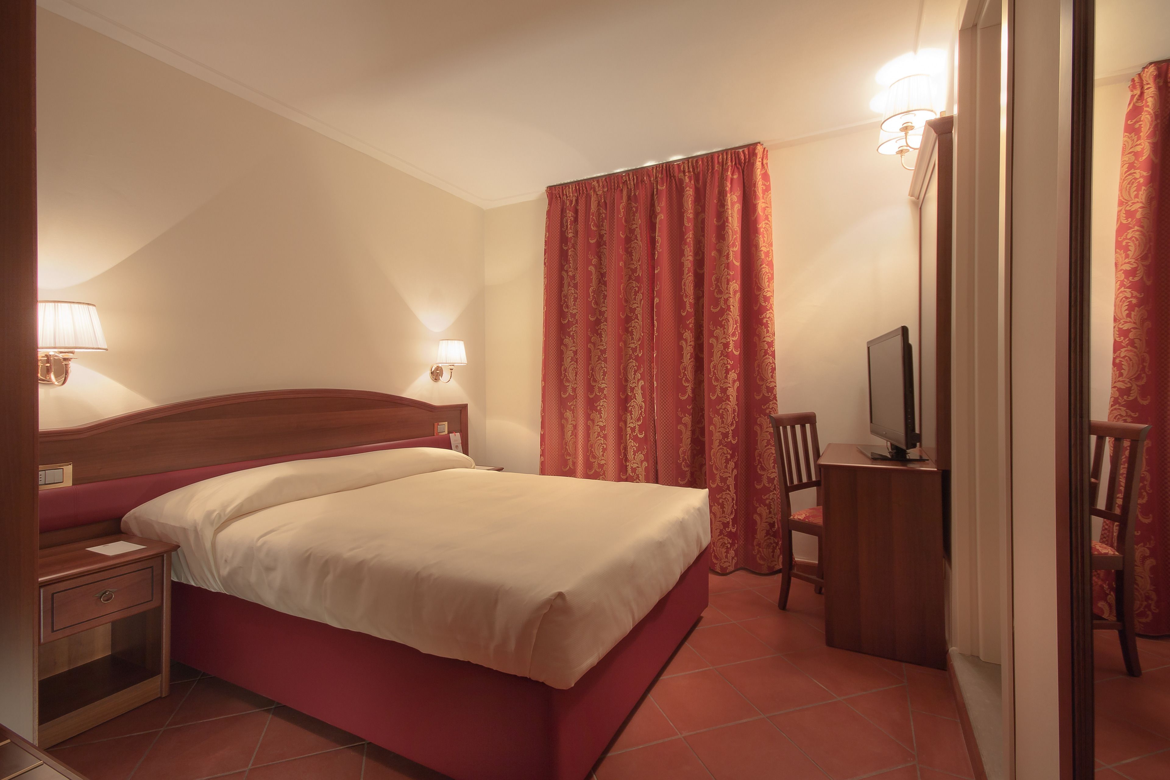 Een hotelkamer met een bed, nachtkastje, lamp, televisie en een stoel.