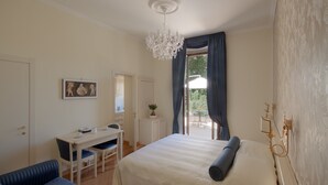 A bedroom with a bed, a desk, and a chair. There is a balcony with a view of greenery. - Relais la Corte di Cloris (Florence)