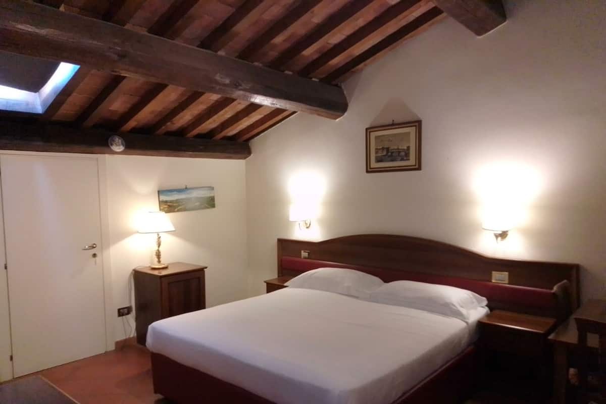 A bedroom with a wooden ceiling, a bed with white linens, two bedside lamps, and a painting on the wall.