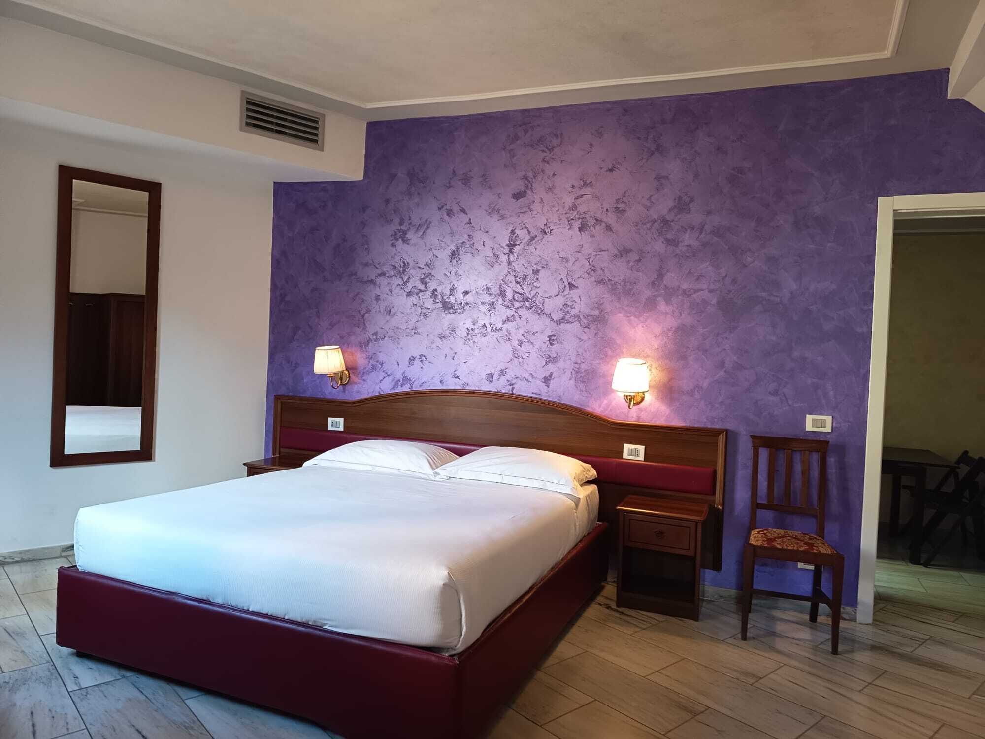 A hotel room with a large bed, two bedside lamps, a wooden nightstand, and a chair.