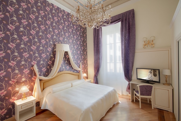 Un dormitorio con cama, mesita de noche, escritorio, silla, televisor y candelabro.