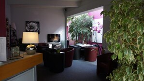 A modern living room with a sofa, a coffee table, and a TV. There is a large window with a view of a garden. - Hotel Restaurant Charme en Beaujolais (Belleville-en-Beaujolais)