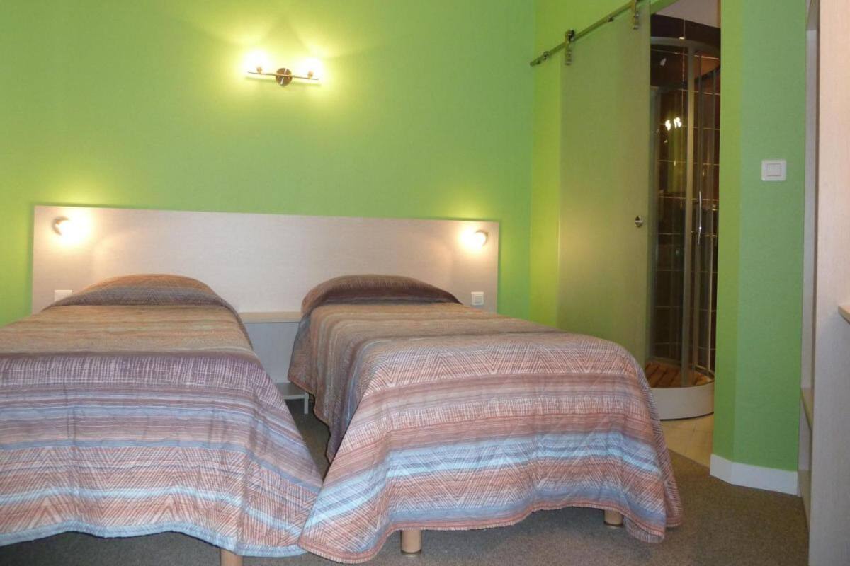 Une chambre avec deux lits, un mur vert et un espace douche.