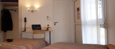 A hotel room with two beds, a desk with a computer, a coat rack, and a door with a poster.