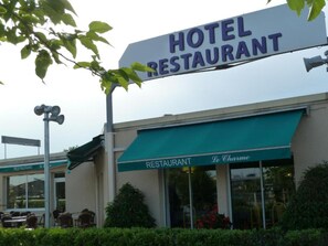 Ein Hotelrestaurant mit Schilder, Außenbestuhlung und einer grünen Markise.