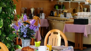 A breakfast setup with a croissant, coffee, and orange juice on a tray, a newspaper, and a vase of purple flowers. - Hotel Restaurant Charme en Beaujolais (Belleville-en-Beaujolais)