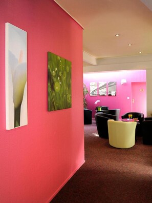 Ein modernes Interieur mit einer leuchtend pinken Wand, einem abstrakten grünen Gemälde und einer Sitzecke mit schwarzen und gelben Stühlen.