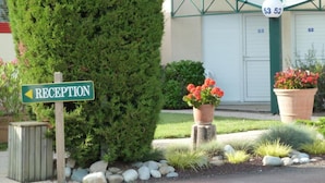 A reception area with a sign, a tall coniferous tree, and a building with garage doors numbered 53 and 52. - Hotel Restaurant Charme en Beaujolais (Belleville-en-Beaujolais)