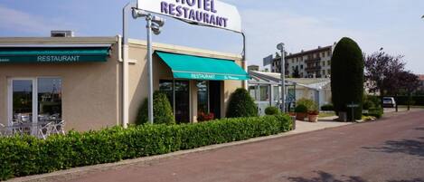 A hotel restaurant with a green awning, outdoor seating, and a clear sky.
