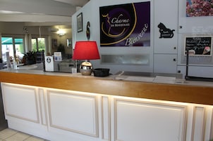 A hotel reception desk with a red lamp, a sign reading 'Charme en Beaujolais,' and a menu board.