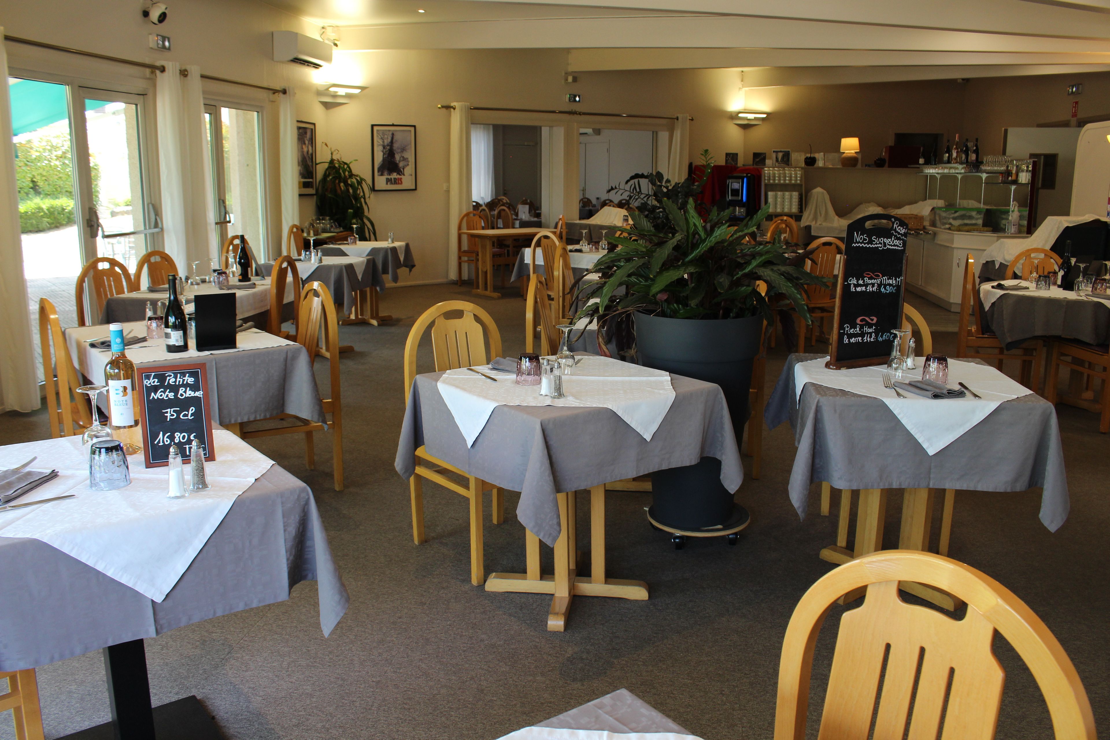 Un interior de restaurante con varias mesas, sillas y una planta grande en maceta.