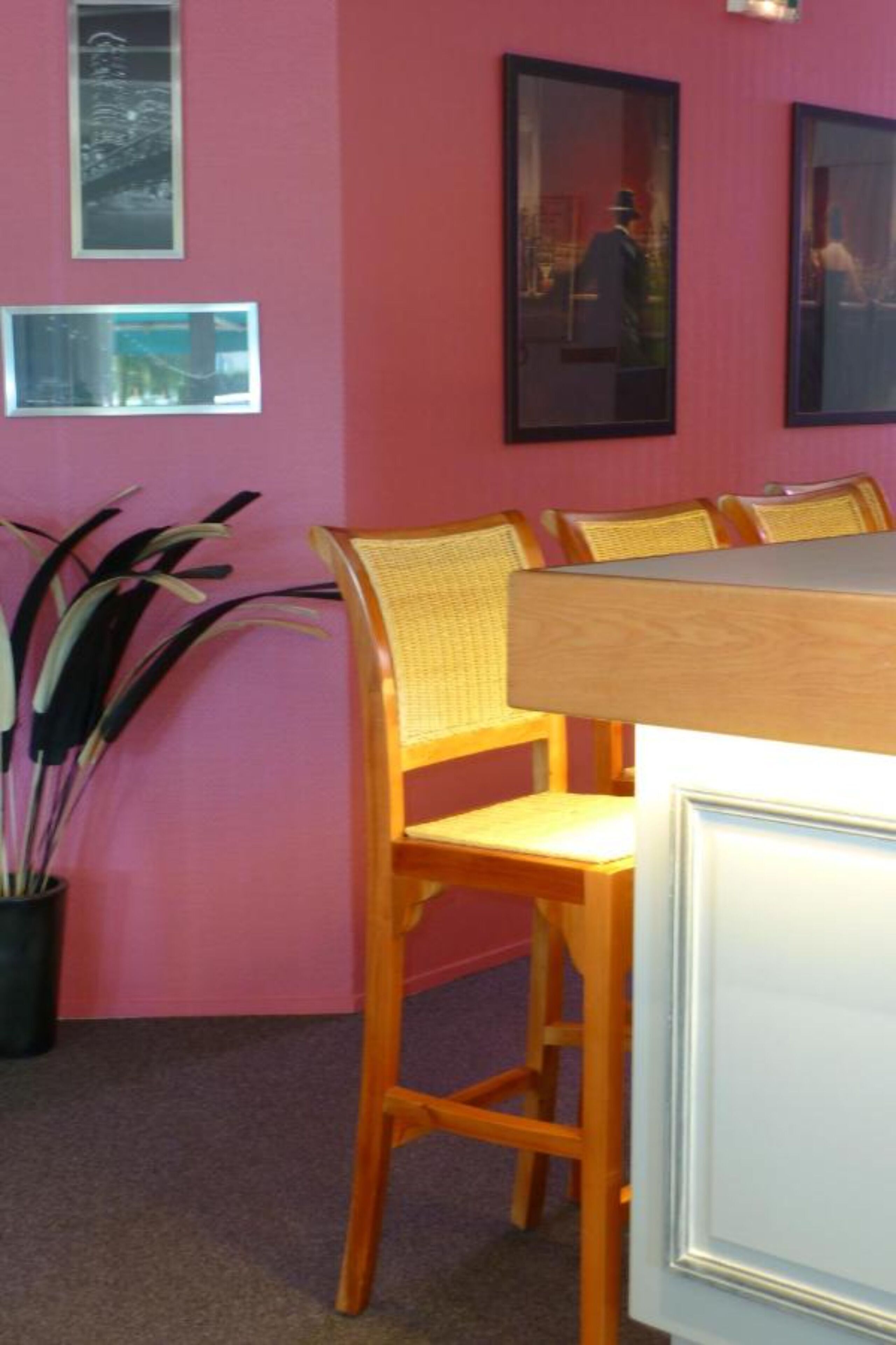 Een eetruimte met een roze muur, ingelijste foto's en rieten stoelen.