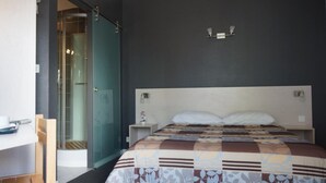 A hotel room with a bed, a desk, and a glass shower enclosure. - Hotel Restaurant Charme en Beaujolais (Belleville-en-Beaujolais)