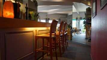 Un vestíbulo de hotel con una recepción, sillas de madera y vistas al comedor.