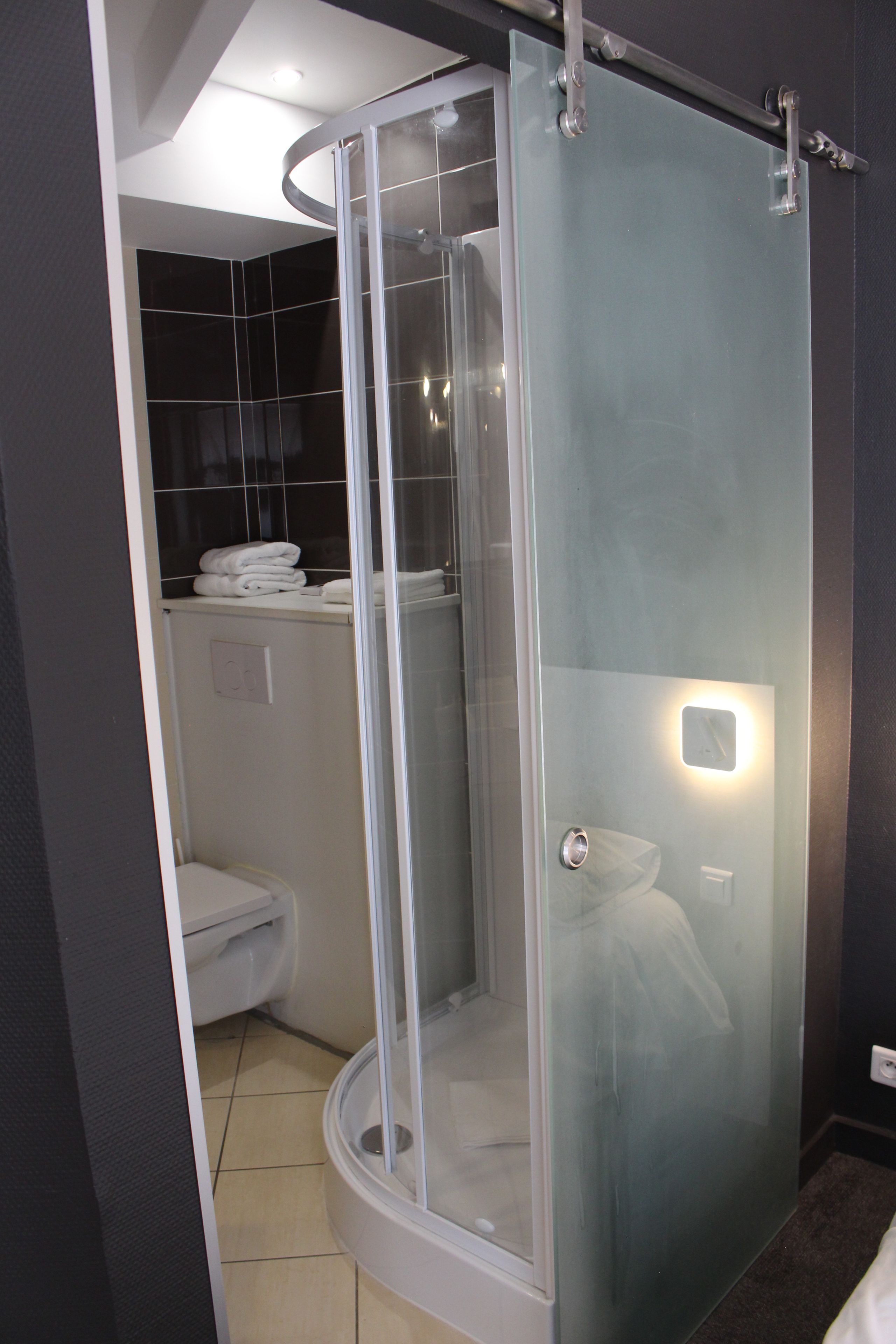 Een moderne badkamer met een douchecabine van glas, een toilet en een handdoekhouder.