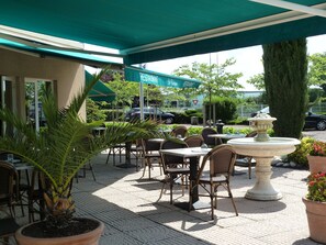 Uma área externa com mesas e cadeiras, uma fonte de pedra e uma placa para 'Le Moulin Restaurant'.