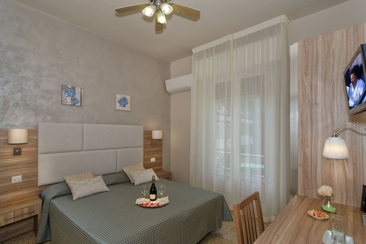 A hotel room with a bed, bedside tables, a TV, a dining table, and a ceiling fan.