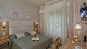 Una habitación de hotel con cama, mesitas de noche, televisor, mesa de comedor y ventilador de techo.